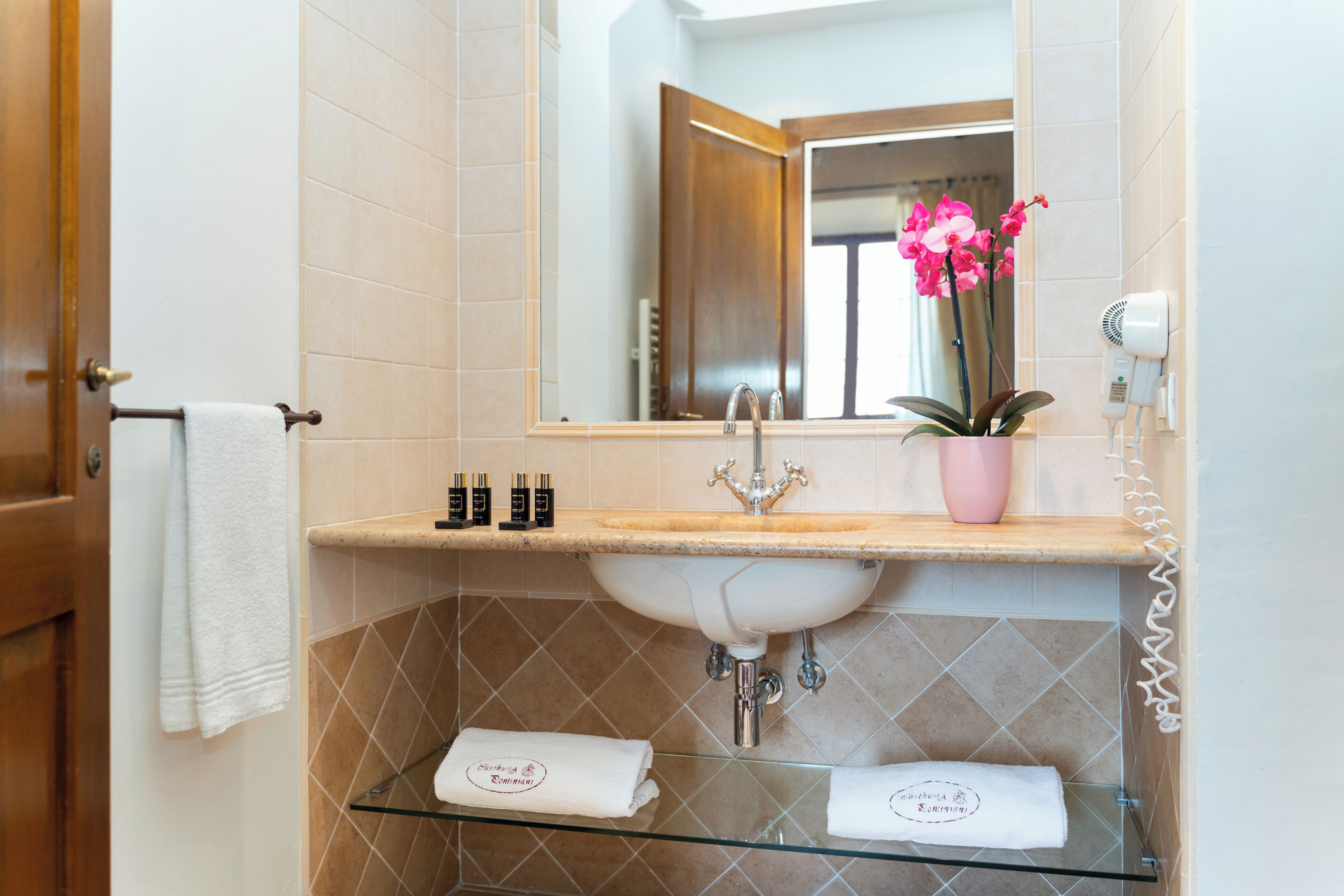 A bathroom with a sink, mirror, towel rack, and a glass shelf with toiletries.