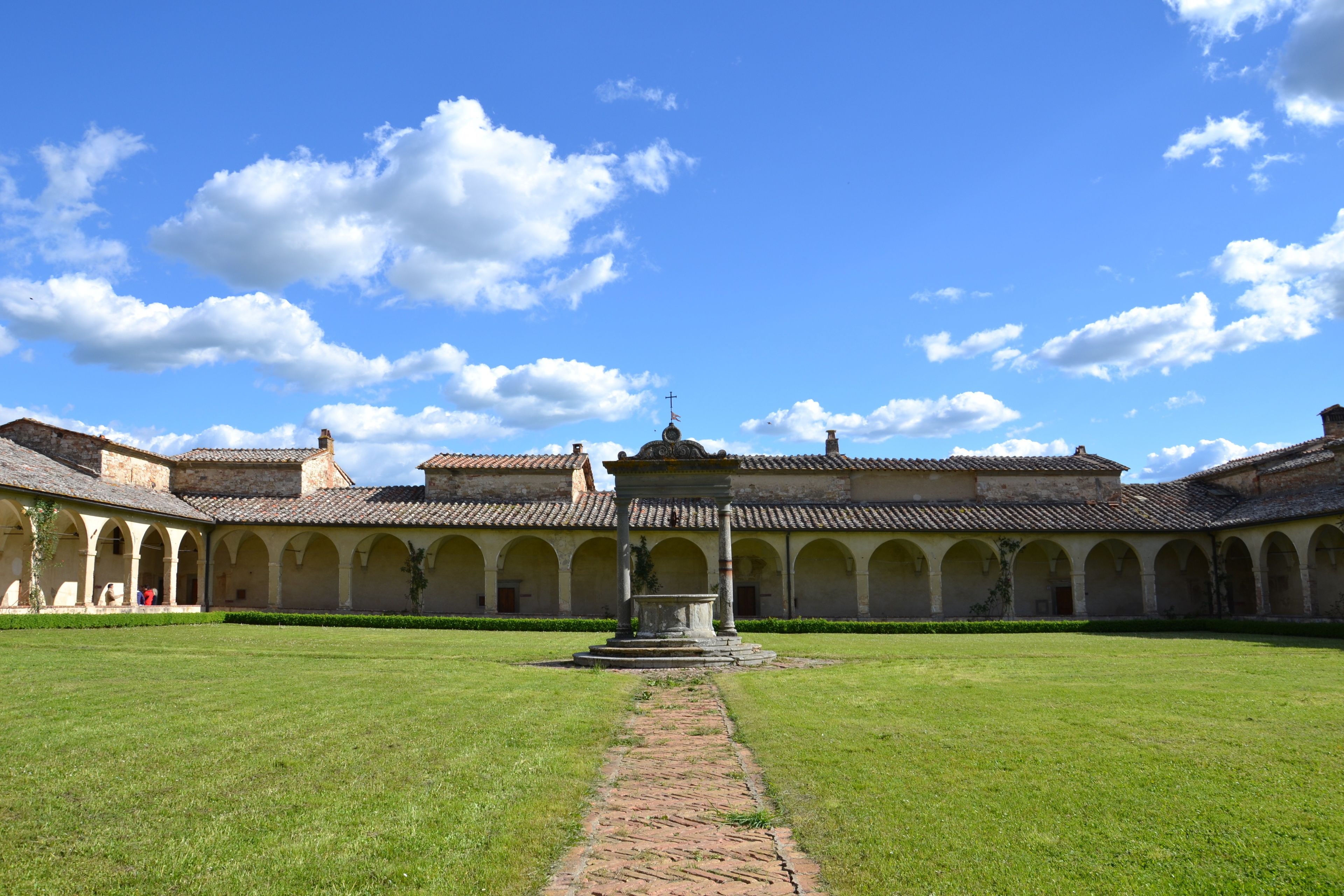 Une cour intérieure avec une fontaine centrale, entourée d’un bâtiment doté de nombreuses arcades et d’un toit en tuiles.