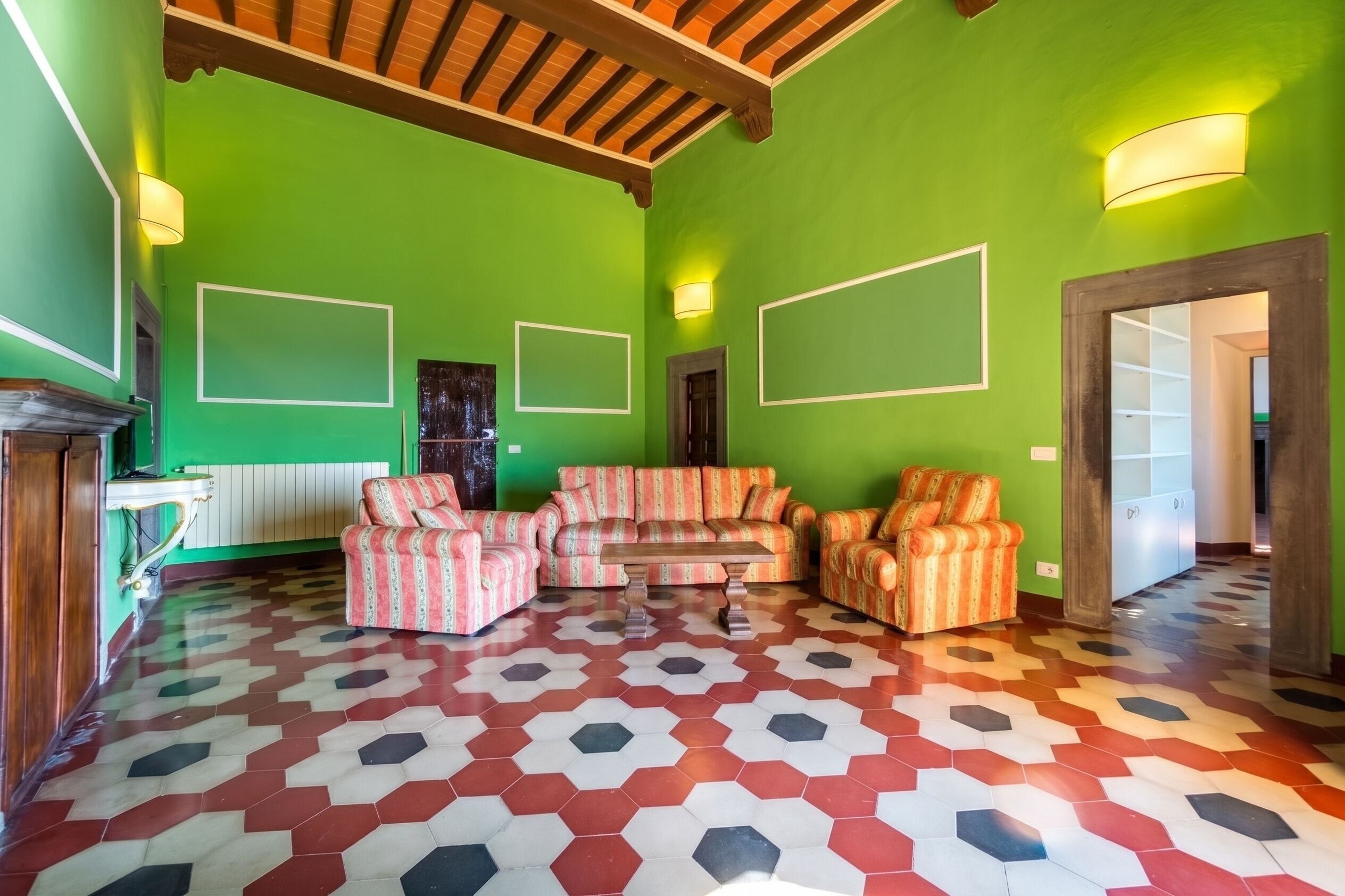 Una habitación con paredes verdes, piso estampado y techo de madera. Hay dos sofás y una mesa.