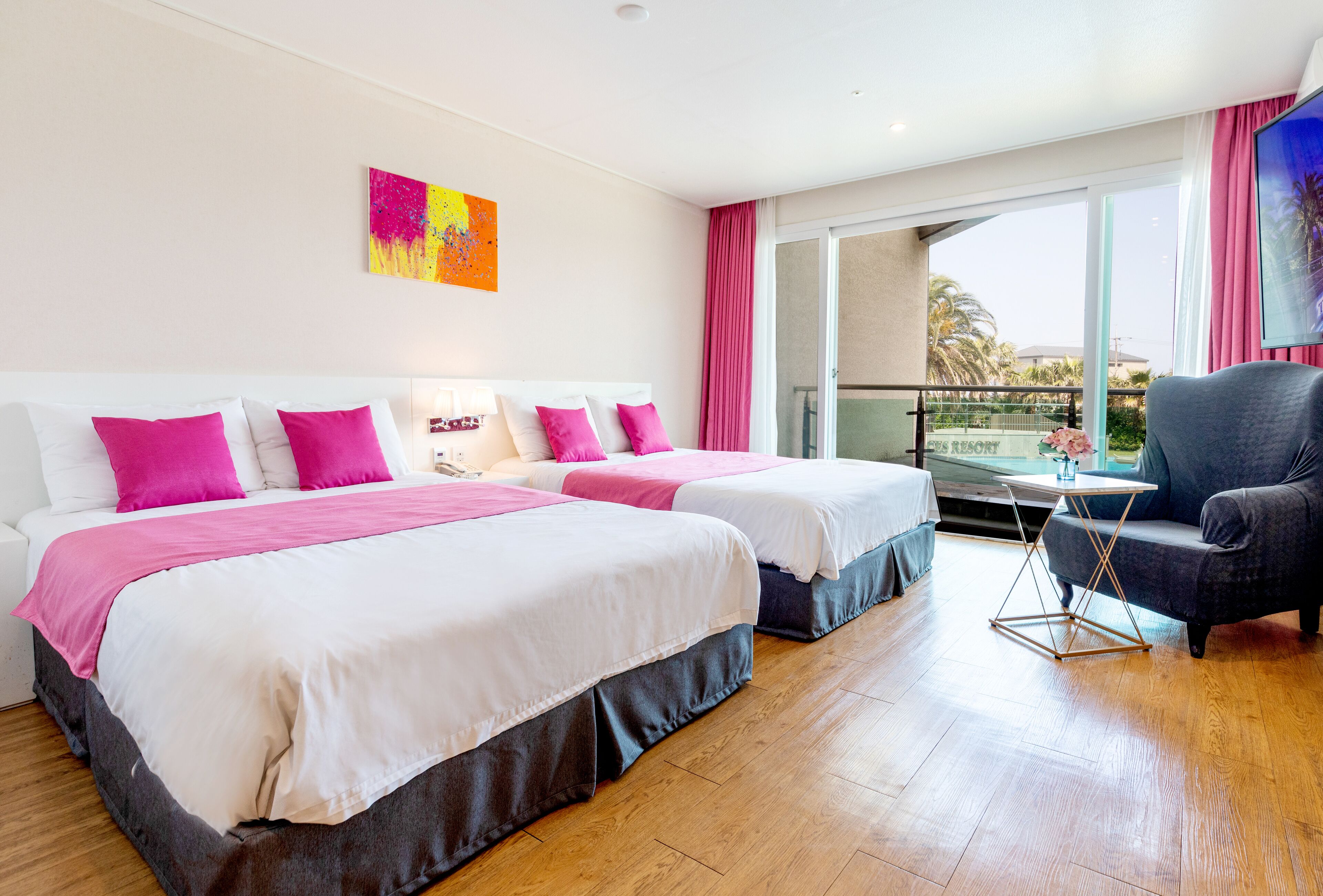 A hotel room with two beds, a chair, a table, and a balcony with a view.
