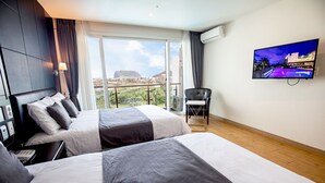 A hotel room with two beds, a TV, and a balcony with a view of a cityscape. - The Four Graces Resort (Seogwipo)