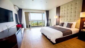 A hotel room with a large bed, a TV, a desk, and a balcony with a view. - The Four Graces Resort (Seogwipo)