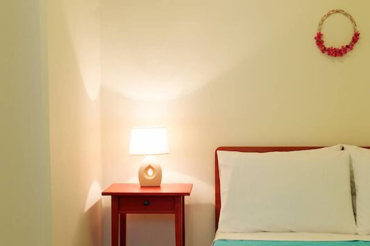 A bedroom with a bed, a nightstand with a lamp, and a wall decoration.