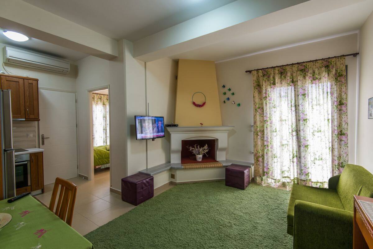 A living room with a fireplace, a television, and a dining area with a green tablecloth.