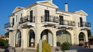 A two-story building with a symmetrical facade, large arched windows, and a central chimney. - Ilida Kourouta Studios (Ilida)