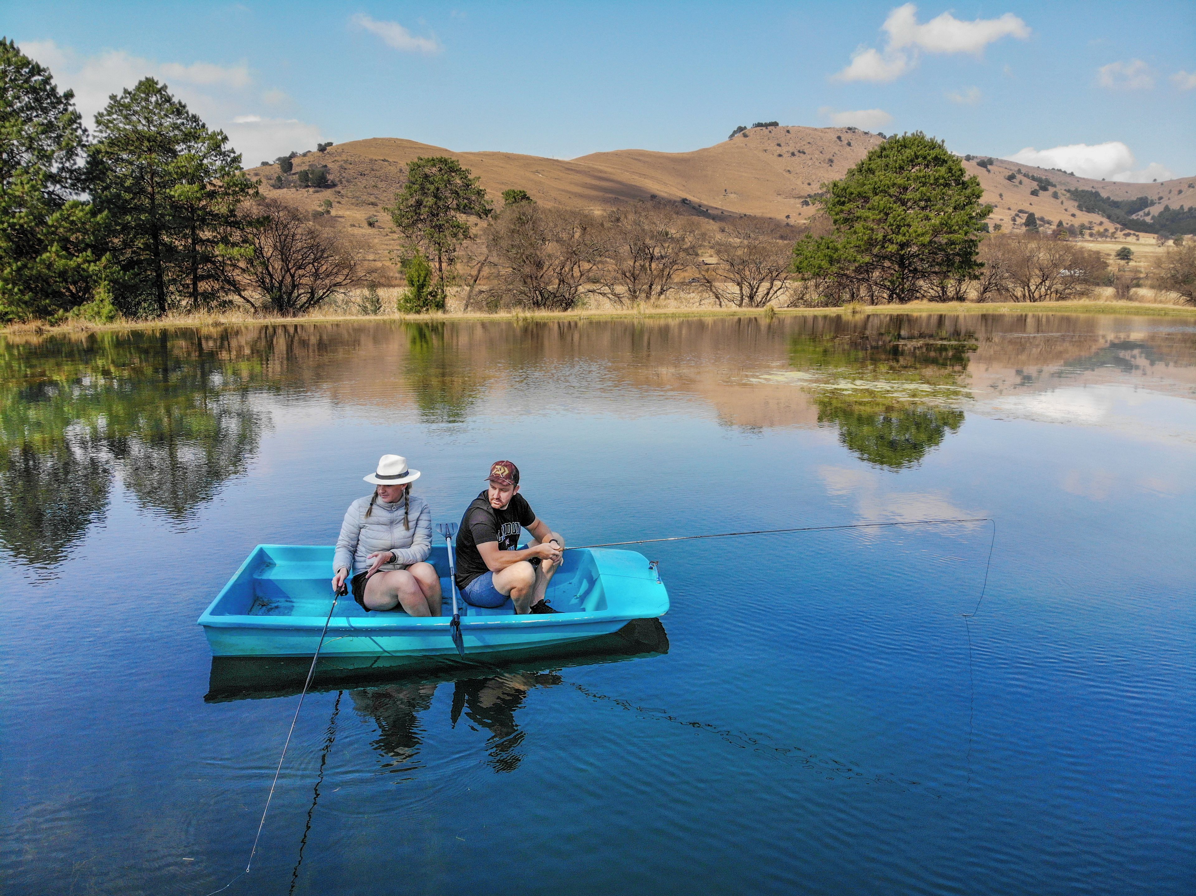 Two people in a small boat on a calm lake with hills in the background.