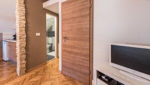 A modern kitchen with a stone pillar, a wooden door, and a flat-screen TV on a white cabinet. - Apartments Donat Zadar (Zadar)