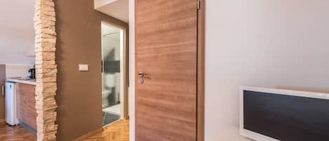 A modern kitchen with a stone pillar, a wooden door, and a flat-screen TV on a white cabinet.
