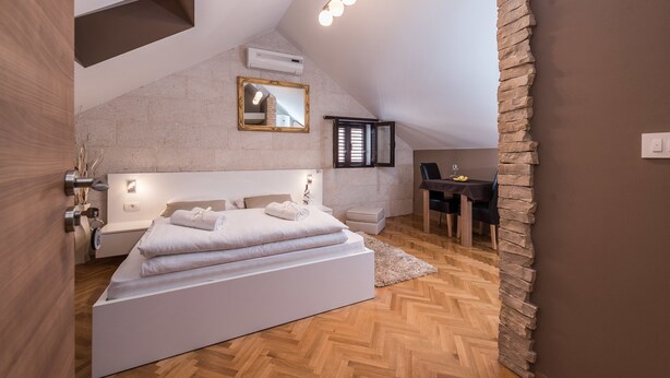 A modern bedroom with a loft-style ceiling, a large bed, a desk, and a stone accent wall. - Apartments Donat Zadar (Zadar)