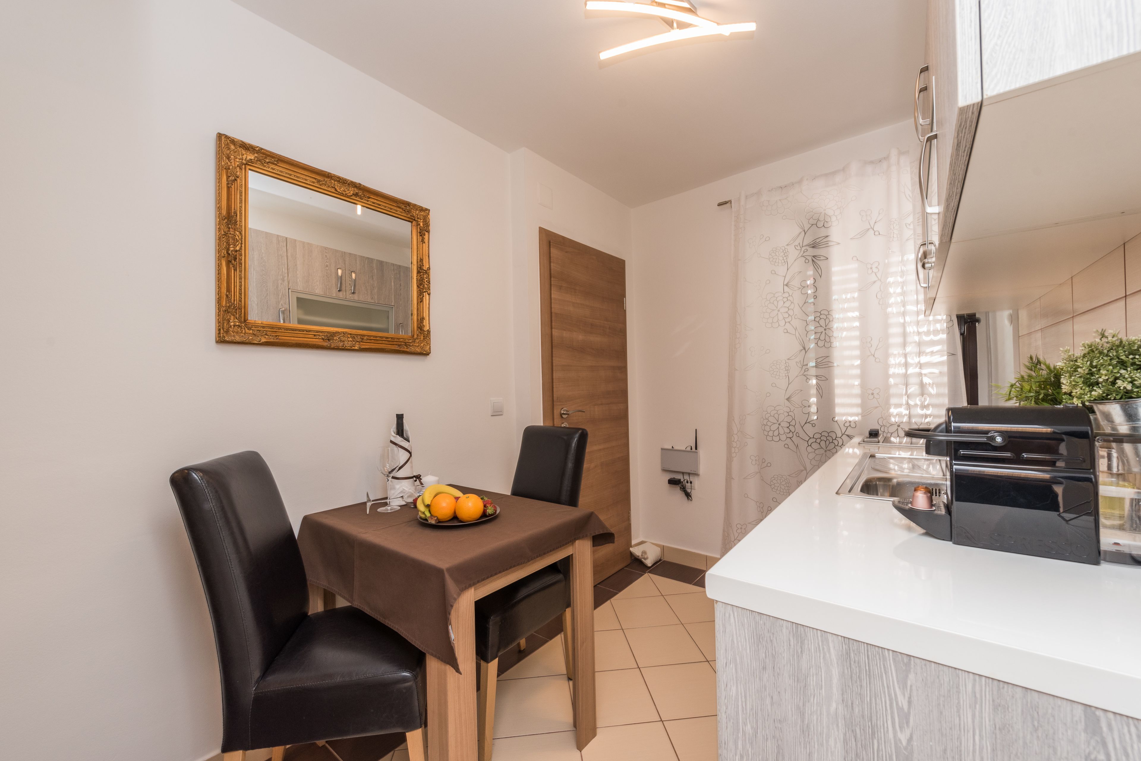 A modern kitchen with a white countertop, a built-in oven, and a dining area with a table and chairs.