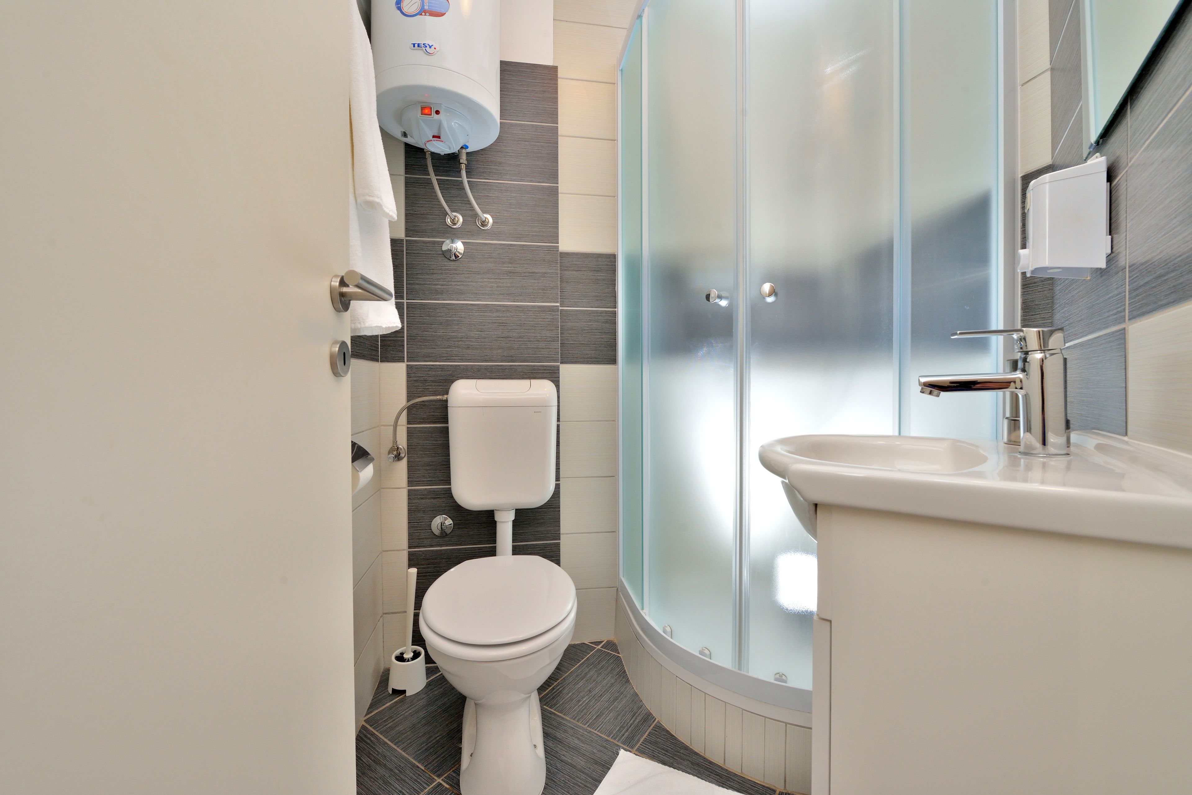 Un baño moderno con inodoro, ducha con mampara de vidrio y lavamanos.