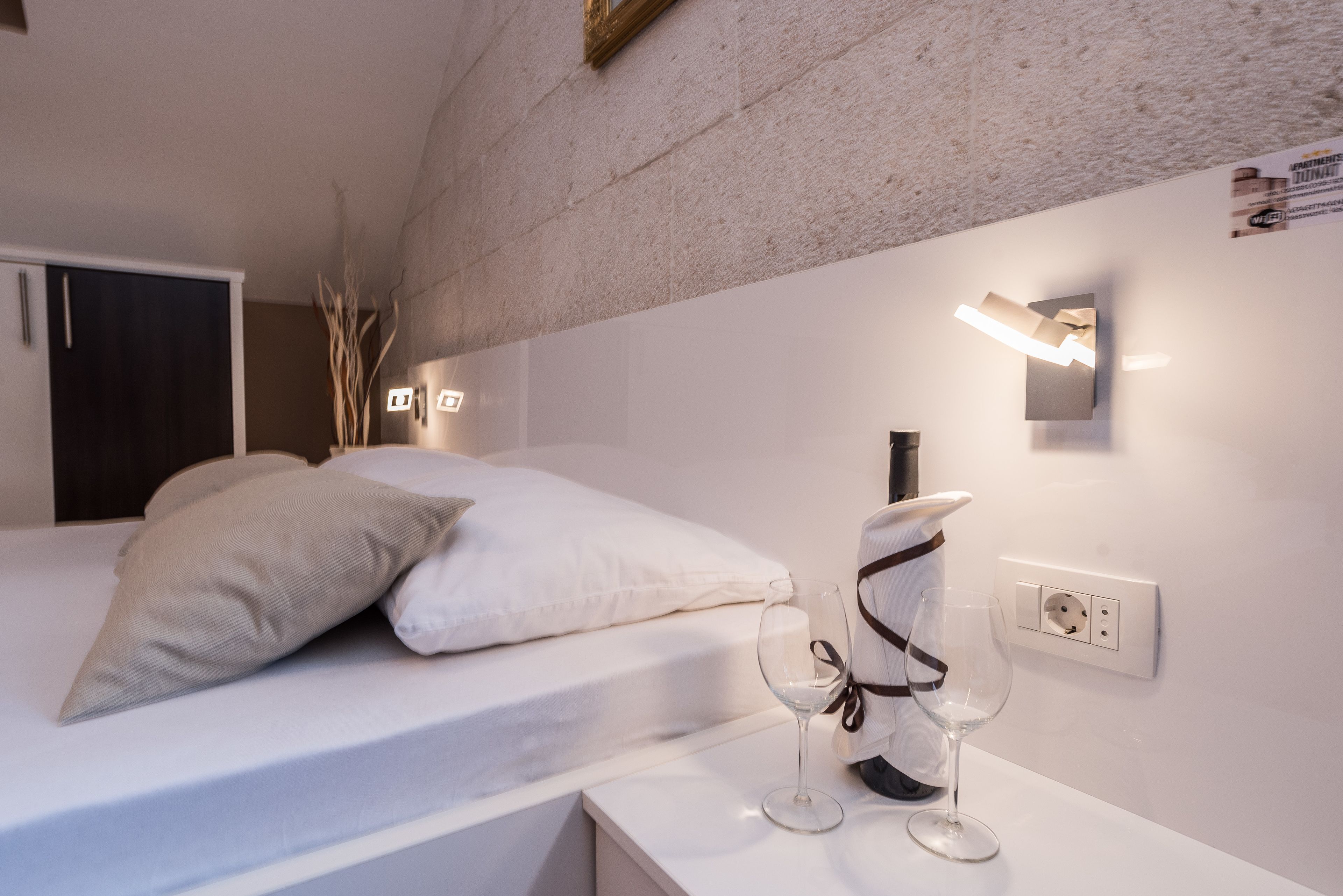 A modern bedroom with a bed, bedside table, and wall-mounted light fixture.