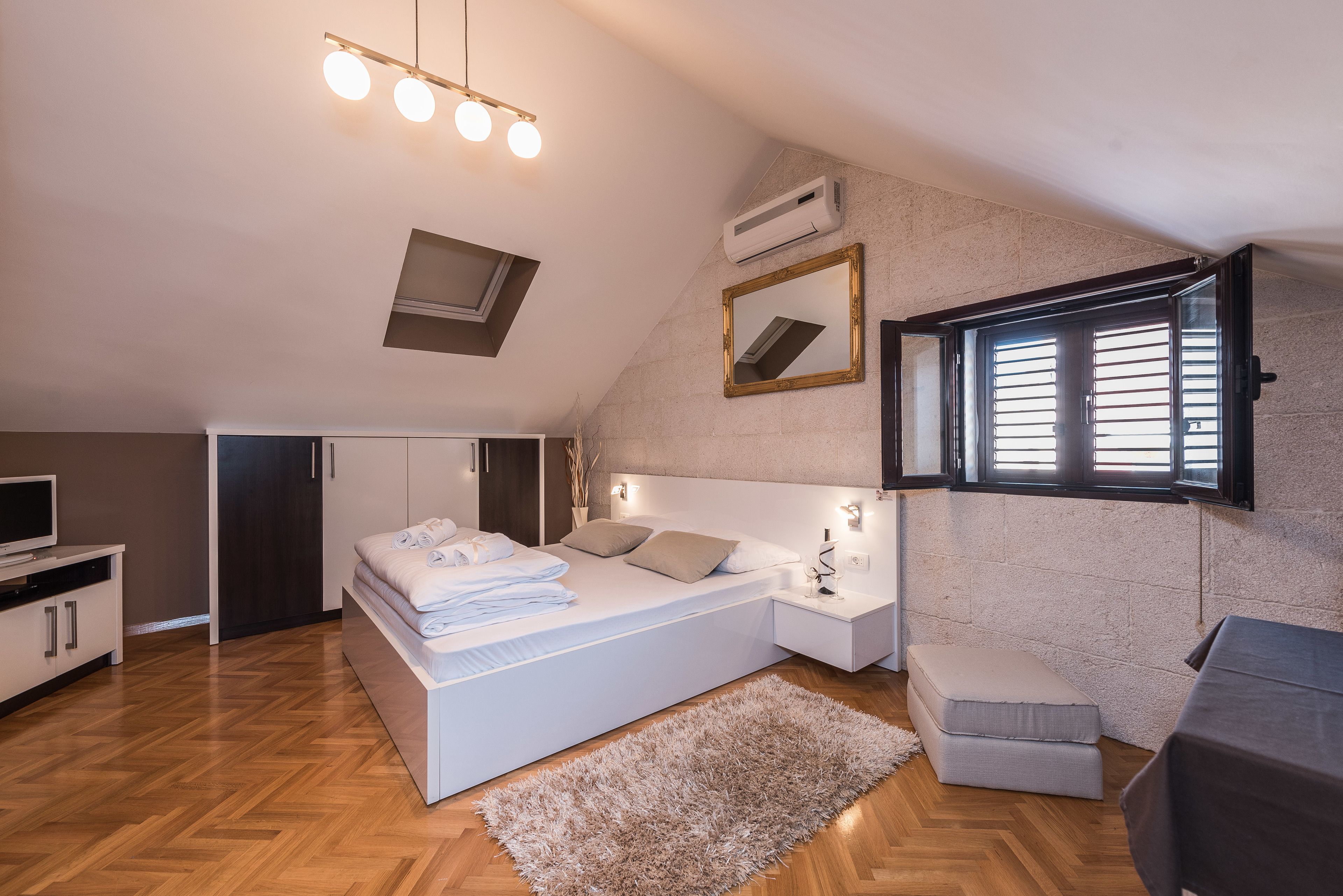 Un dormitorio con una cama grande, mesitas de noche, televisión y ventana con contraventanas.