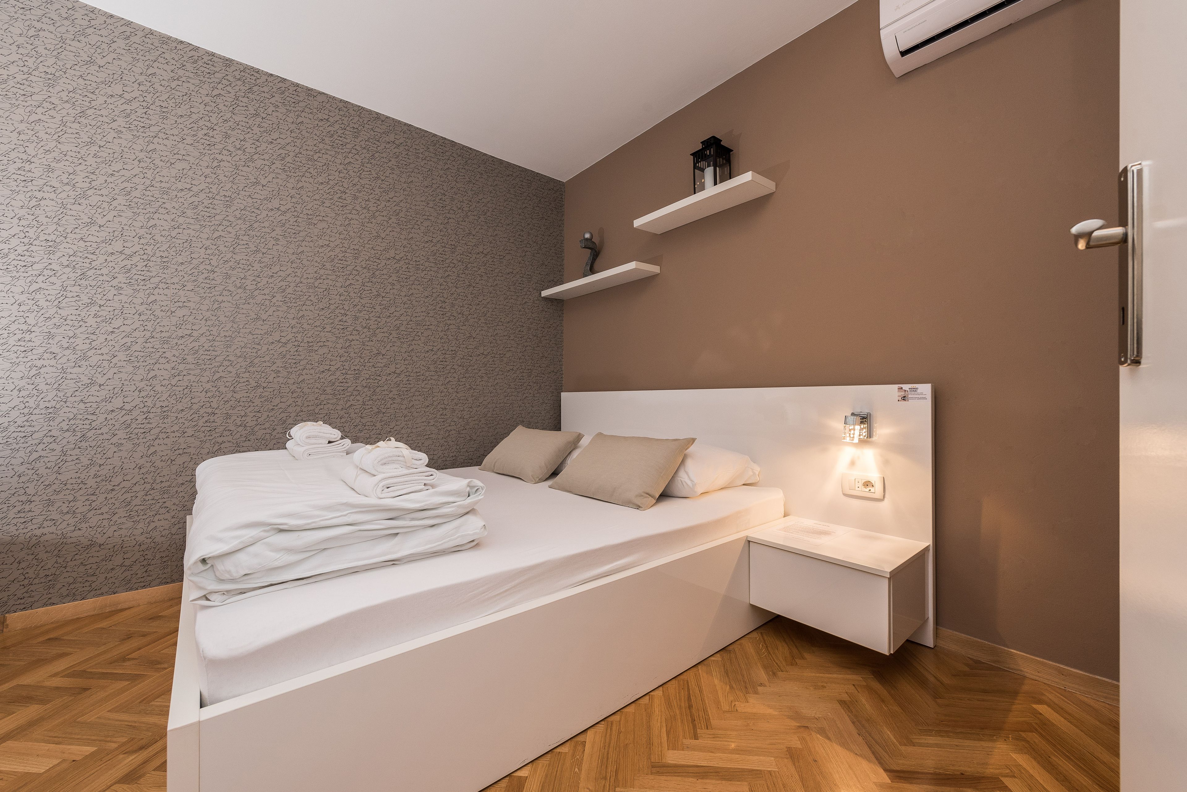 A modern bedroom with a bed, bedside table, and wall-mounted shelves.