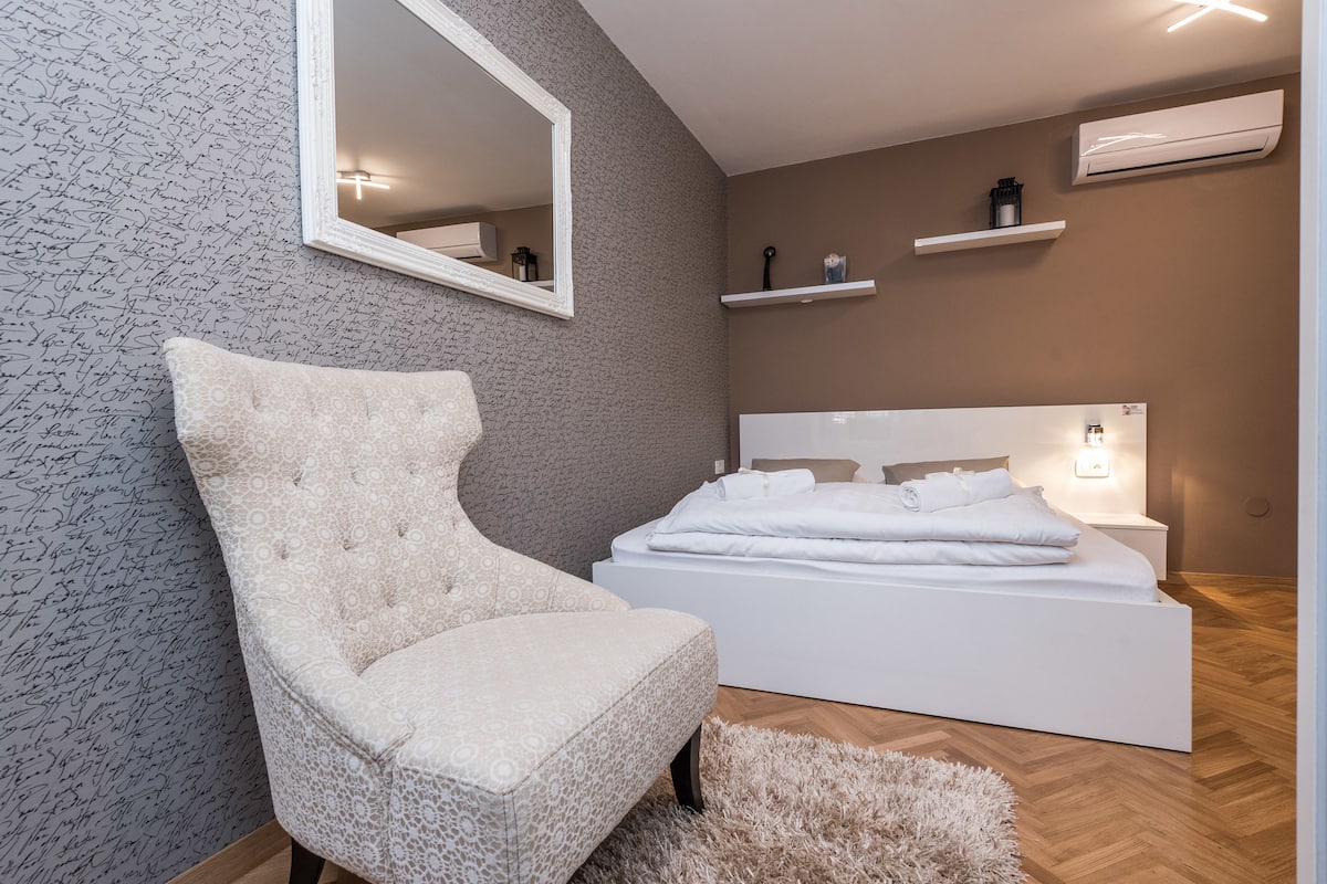 Ein Schlafzimmer mit einem großen Bett, einem Sessel, einem Spiegel und einer Wand mit einem markanten Muster.