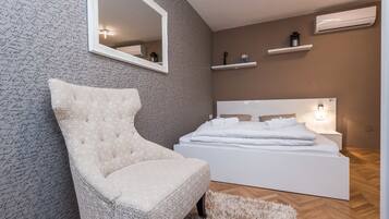 A bedroom with a large bed, a chair, a mirror, and a wall with a signature pattern.