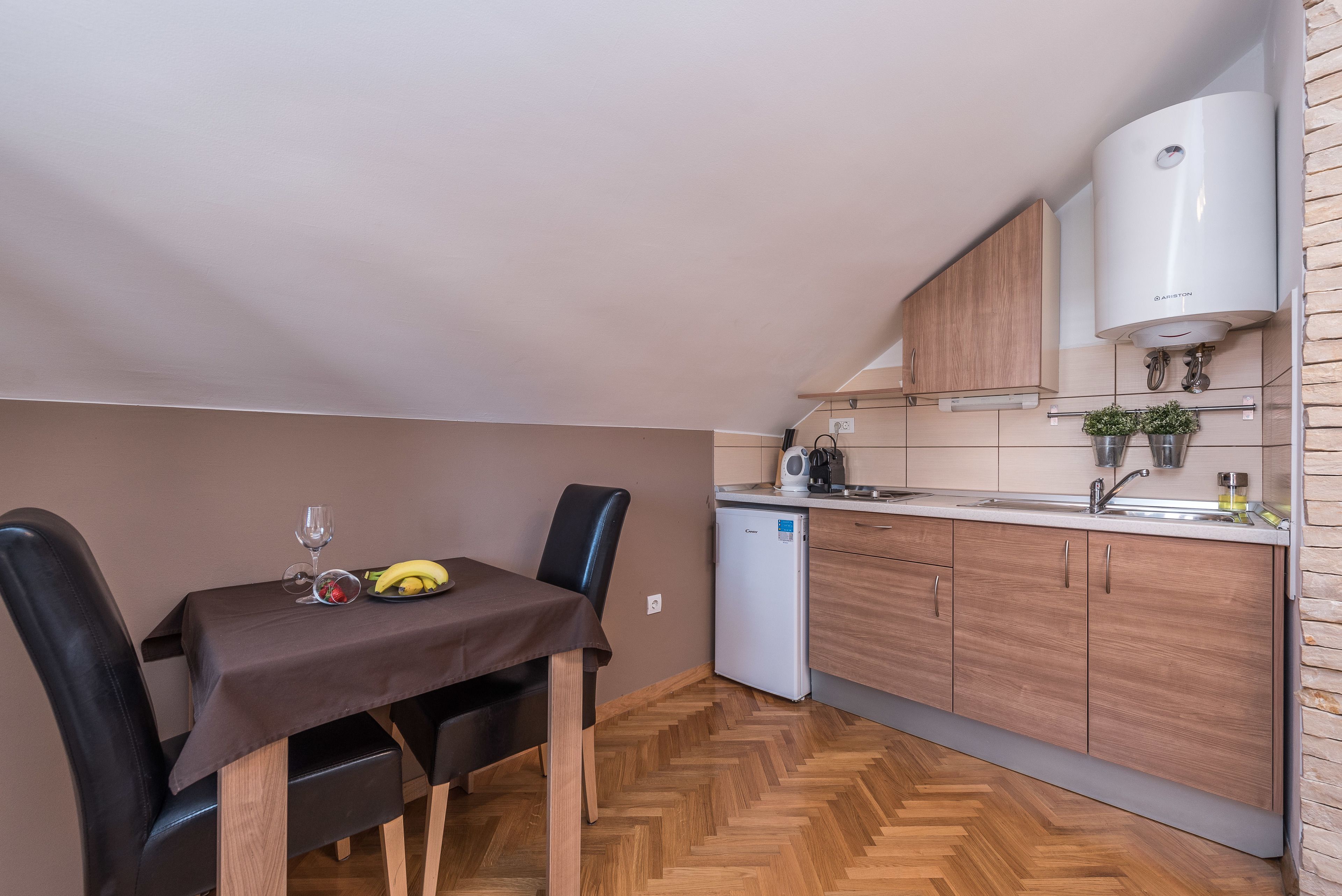 Une cuisine compacte avec un coin repas, dotée d’un parquet en bois disposé en chevrons, d’un petit réfrigérateur et d’un four à micro-ondes encastré.