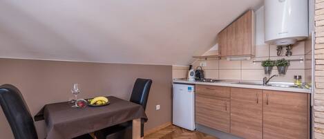 Une cuisine compacte avec un coin repas, dotée d’un parquet en bois disposé en chevrons, d’un petit réfrigérateur et d’un four à micro-ondes encastré.