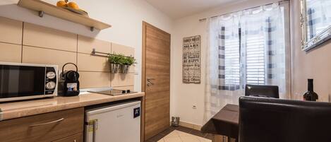 A modern kitchen with a microwave, coffee maker, and a small refrigerator. There is a dining table with chairs and a window with curtains.