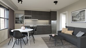 A modern kitchen with dark cabinets, a white countertop, and a stainless steel refrigerator. There is a dining area with a white table and black chairs. A gray sofa with patterned cushions is in the living area. - Naantali City Apartments (Naantali)