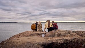 Four people sitting on a rocky shore overlooking a body of water. - Naantali City Apartments (Naantali)