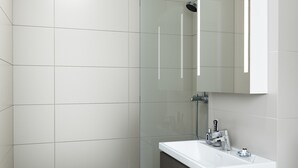 A modern bathroom with a shower, a sink with a mirror, and a toilet. - Naantali City Apartments (Naantali)