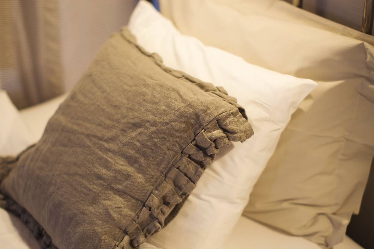 Ein Bett mit weißen Leinentüchern und einem braunen Kopfkissen.