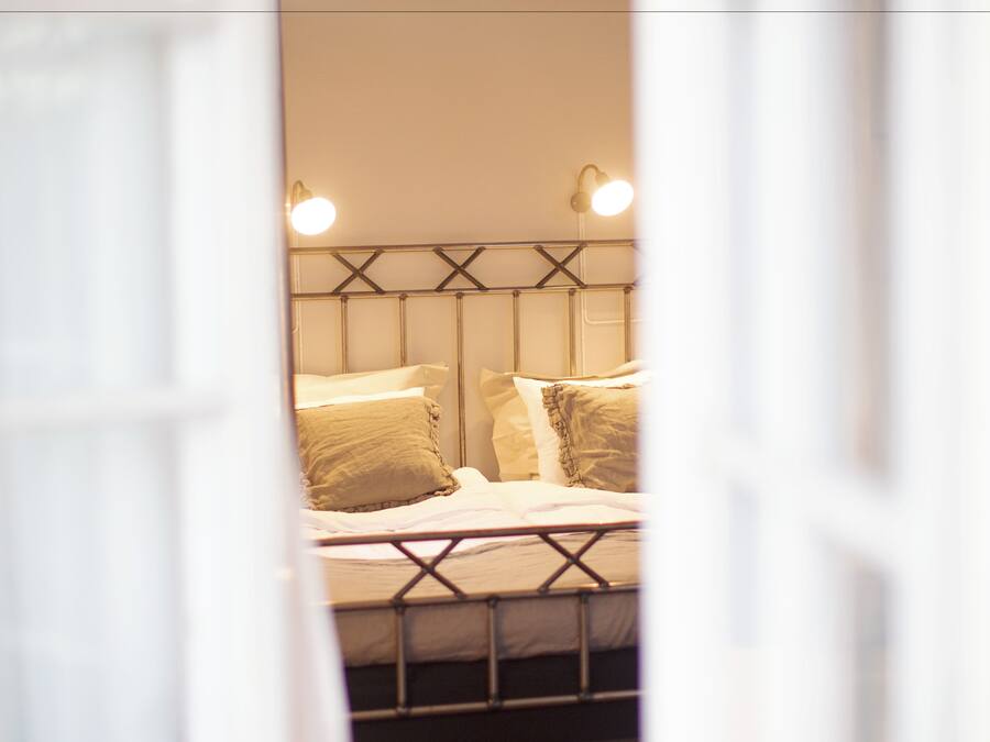 Quarto com cama, abajures e um banquinho.