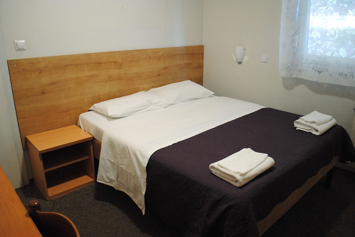 A single bed with a wooden headboard, a nightstand, and a window with a floral curtain.