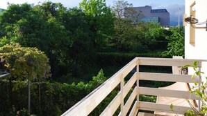 A wooden balcony with a view of lush greenery and a modern building in the background. - Hotel Fala (Zagreb)