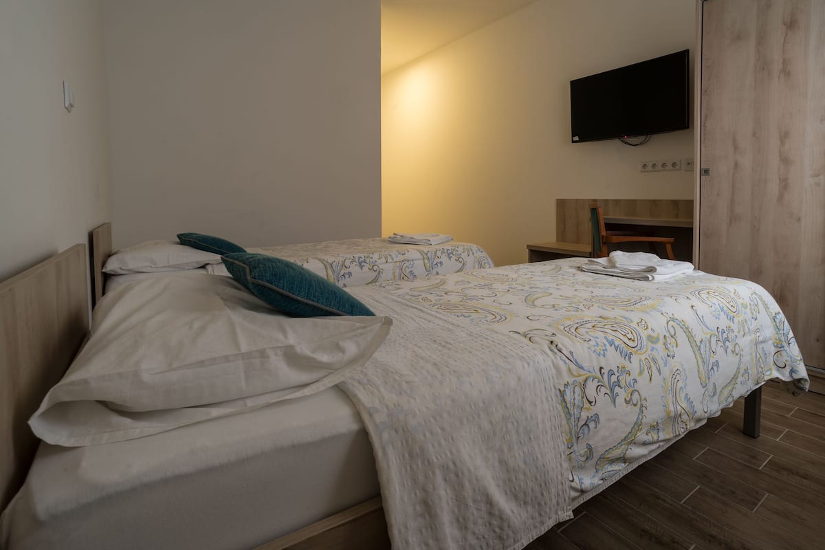 A bedroom with two beds, a TV mounted on the wall, and a wooden floor.