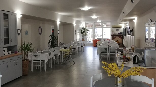 A spacious dining area with multiple tables and chairs, a kitchen area with appliances, and a view of the outdoors. - Hotel Fala (Zagreb)