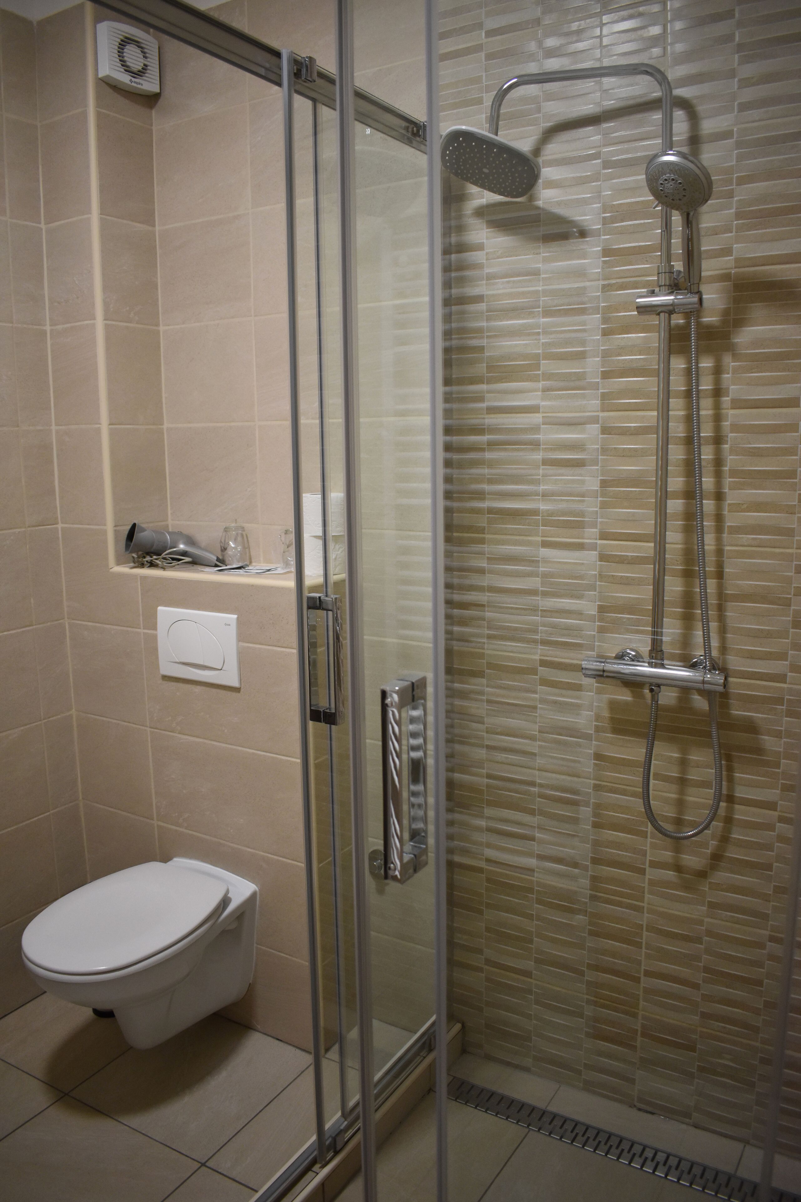 Un baño con ducha de vidrio, inodoro y repisa con artículos de aseo.