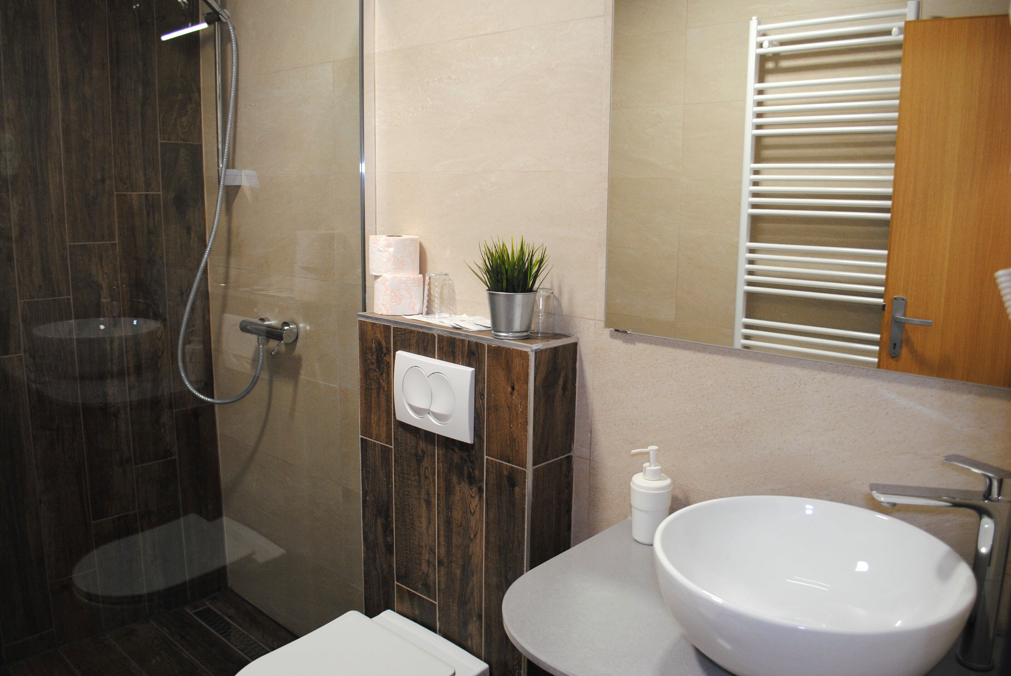 Un baño con ducha envuelta en vidrio, un lavamanos blanco y un tocador de madera.