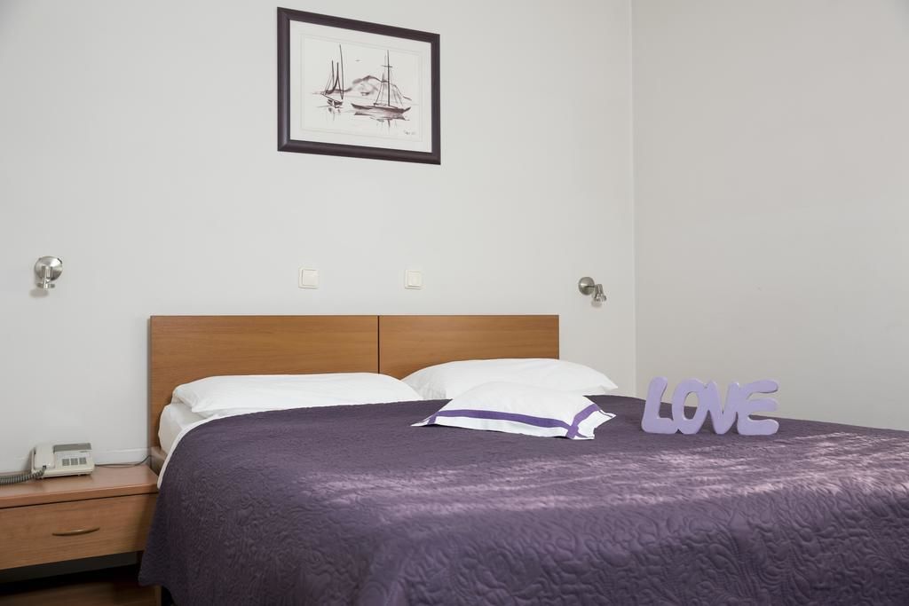 A neatly made bed with a purple bedspread, a framed artwork above it, and a 'LOVE' sign on the bed.