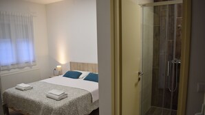 A hotel room with a bed, a bedside table with a lamp, a shower area with glass doors, and a window with curtains. - Hotel Fala (Zagreb)