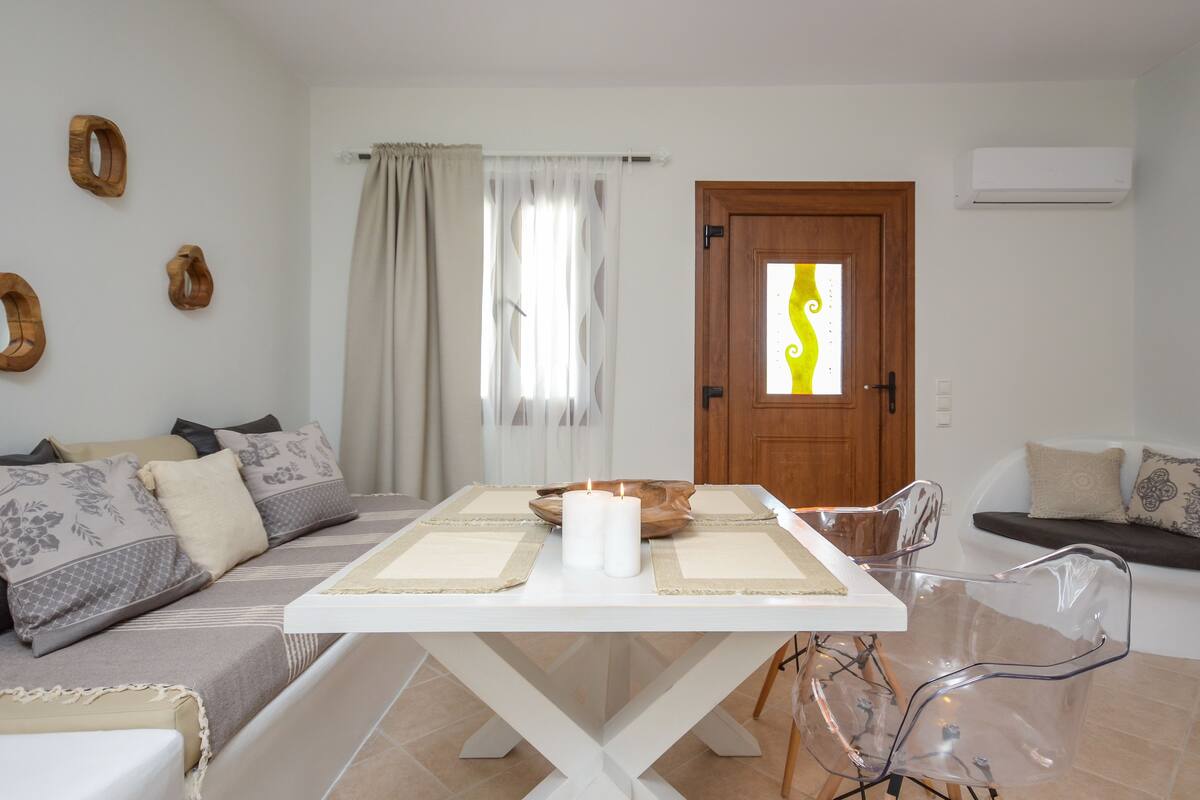 A living room with a white dining table, clear chairs, a sofa, and a wooden door with a glass panel.