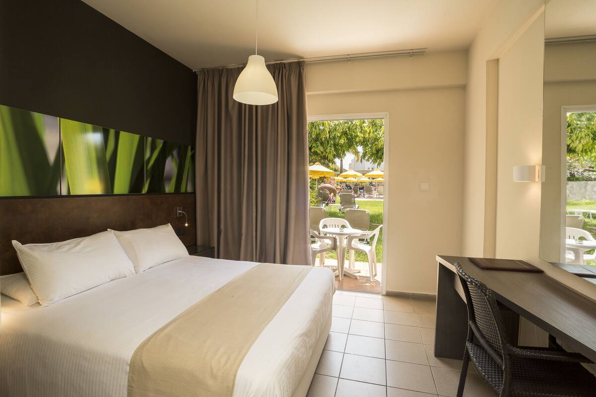 A hotel room with a large bed, a desk, and a view of the outdoor seating area.