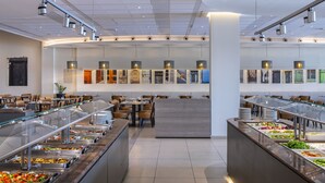 A buffet area with multiple food stations, seating arrangements, and overhead lighting. - Mayfair Gardens (Paphos)