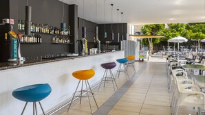 A modern bar area with a white countertop, multiple stools, and a variety of bottles on shelves. - Mayfair Gardens (Paphos)