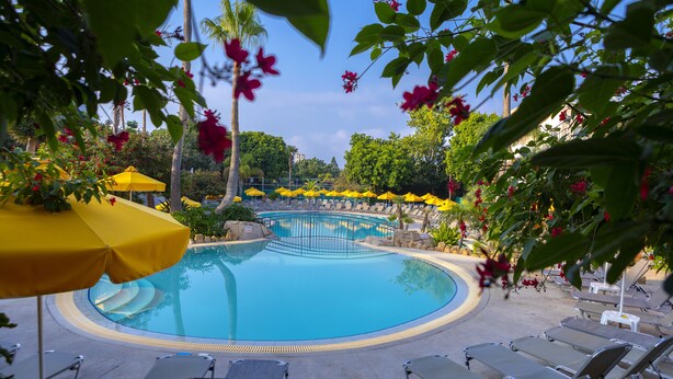 A swimming pool with lounge chairs and yellow umbrellas. - Mayfair Gardens (Paphos)
