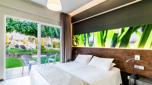A modern hotel room with a large bed, a view of the outdoors, and a wall-mounted TV. - Mayfair Gardens (Paphos)