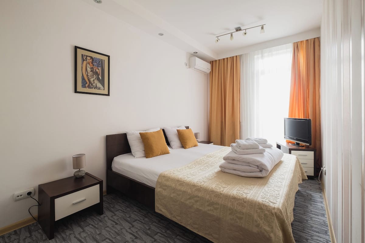 Une chambre d’hôtel avec un lit, une table de chevet, un téléviseur et une fenêtre avec des rideaux.