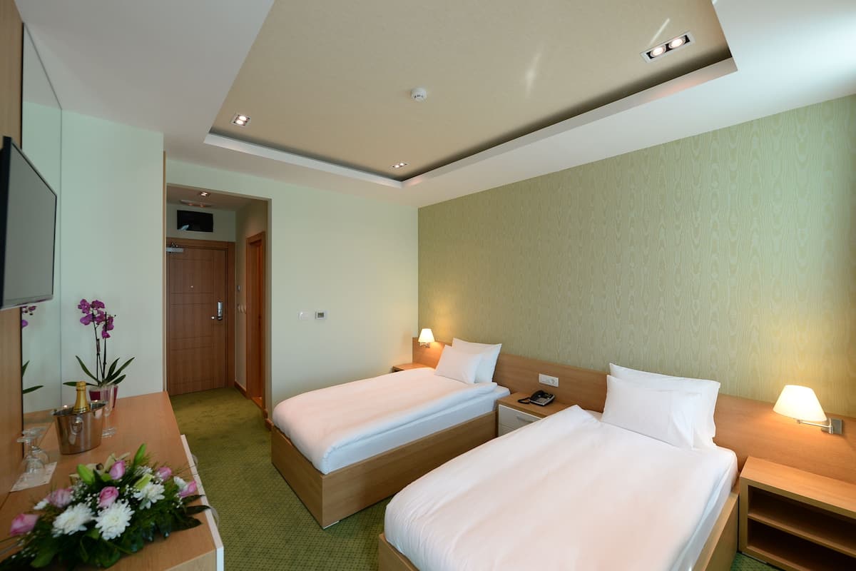 A hotel room with two beds, a desk with a vase of flowers, and a wooden nightstand with a lamp.