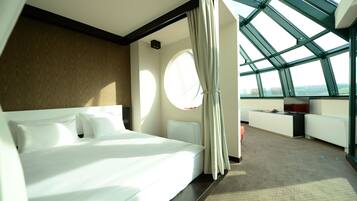 A modern hotel room with a large bed, a seating area with a view, and a skylight.