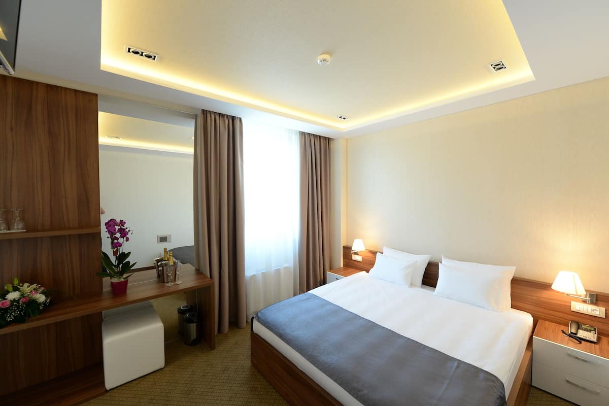 A hotel room with a bed, bedside tables, a desk, a mirror, and a window with curtains.