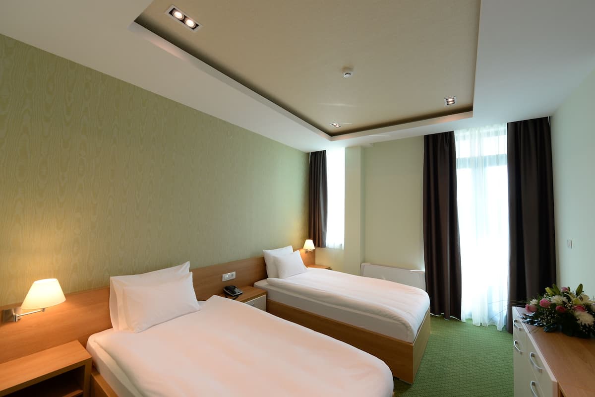 A hotel room with two beds, a desk, a lamp, a telephone, and a window with curtains.
