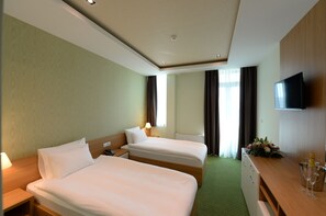 A hotel room with two beds, a desk, a flat-screen TV, and a window with curtains. - Hotel Hedonic (Belgrade)