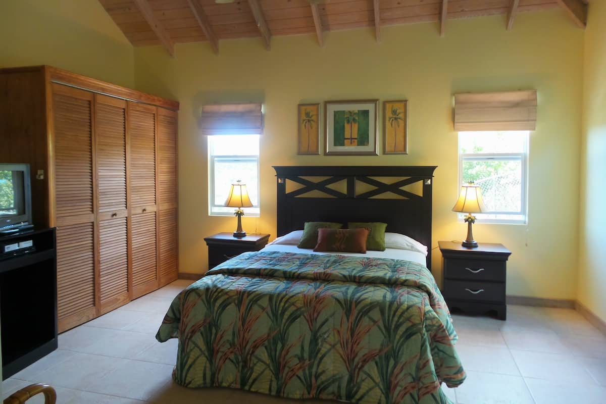 A bedroom with a bed, wooden wardrobe, two bedside tables with lamps, and a ceiling fan.