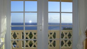 A view through a balcony door with a clear sky and ocean in the background. - South Coast Ocean View Apartments (Cades Bay)
